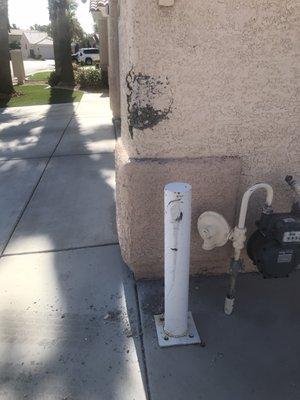 Damaged house wall and gas meter barrier.