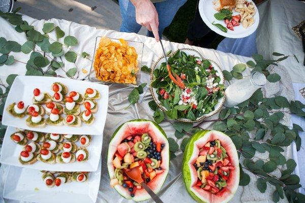 Another view of fruit, salad, appetizers, and potato chips at catering event.