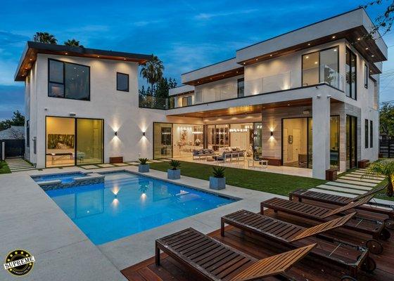 Modern backyard remodel at night with tanning deck, wrap around balcony, swimming pool, custom lighting and a large granite patio.