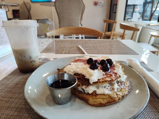 Tiramisu latte with almond milk and a stack of buffalo ricotta pancakes with chocolate and black cherries and a side of syrup.