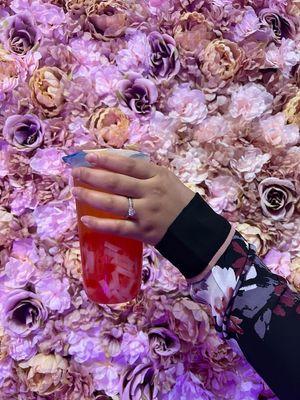 Bubble tea in front of flower wall.