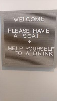 Sign says welcome please have a seat and help yourself to a drink