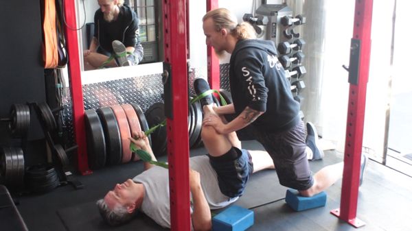 BUF team trainer, Seth, assisting our client, Jay, with a piriformis stretch.