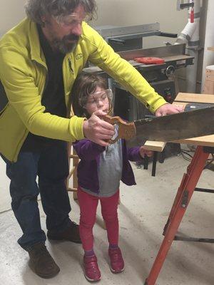 Lucy gets some help sawing a piece of wood to paint on.