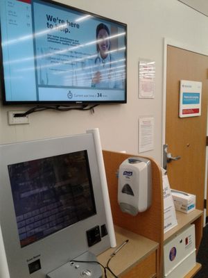 Sign in at kiosk bottom left, upper tv screen shows the wait and door on right is the office.