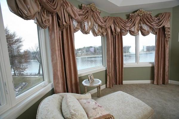 Center raised open swag valances mounted on crest in a large bay window with mock balloon valances and stationary side panels.