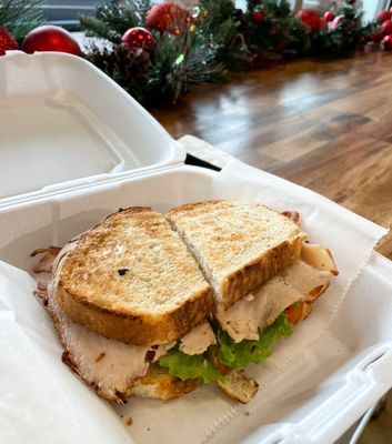 THE TURKEY CLUB: 
 Served on Sourdough, Oven Roasted Turkey, Bacon, Cheddar Cheese, Lettuce and Tomato with Roasted Garlic Aioli.