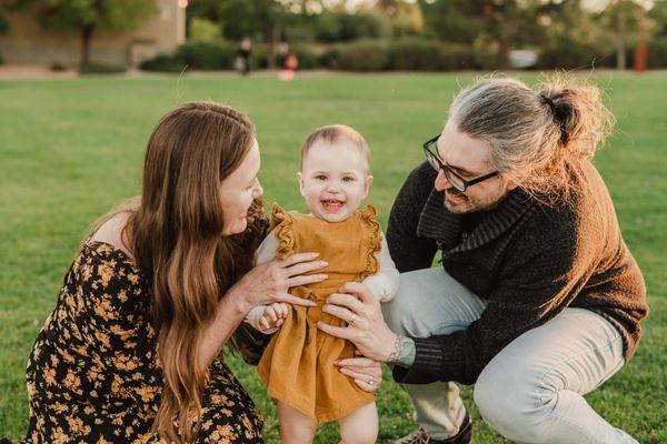 Joyful family of mom and dad running up to their toddler girl in the park during sunset