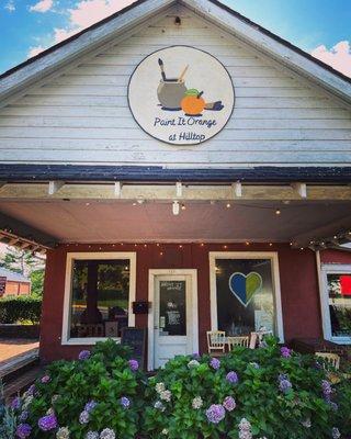 The front of the Paint It Orange studio in Orange Virginia with sign and flowers.