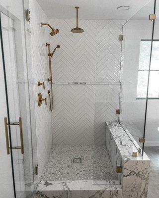 Perfectly exquisite custom shower enclosure with marble, brass shower wand assembly, and rain shower head.