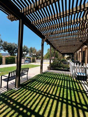 A serene outdoor seating area with wooden pergolas, green grass, and benches, perfect for relaxation and study