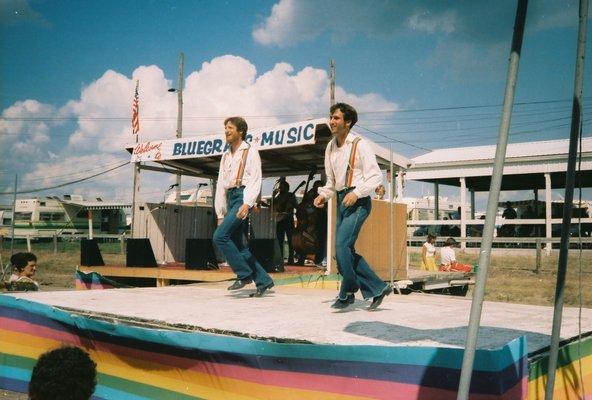 Mark and Tom doing a buck dance at Clark County Fairgrounds.  Other cloggers in yellow and red dresses are in the back of the stage.