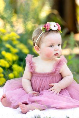 Baby girl wearing a mauve lace dress with a floral headband during a 1st birthday milestone photo session on Texas Tech Campus