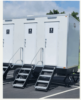 White restroom trailer with black signage, metal stairs with handrails.