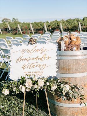 Welcome sign greenery/ flowers. White rose petals in basket