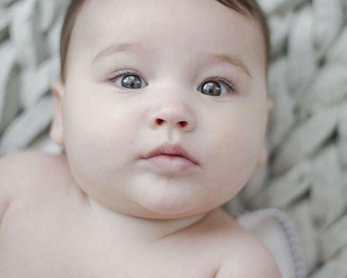 Close-up of baby with big eyes lying on a woven blanket, captured in Sacramento by Cherish the Moment Photography.