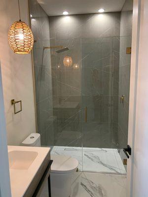 Inline frameless shower door enclosure with brushed gold hardware