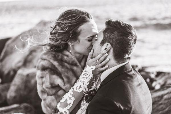 Bride and groom kiss on jetty with ocean in back