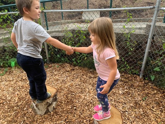 Two friends working hard to  help each other, to stay on the logs with out falling off.