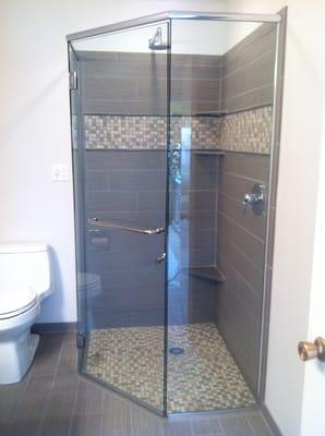 A tile shower with curb-less floor and frameless neo-angle shower door.