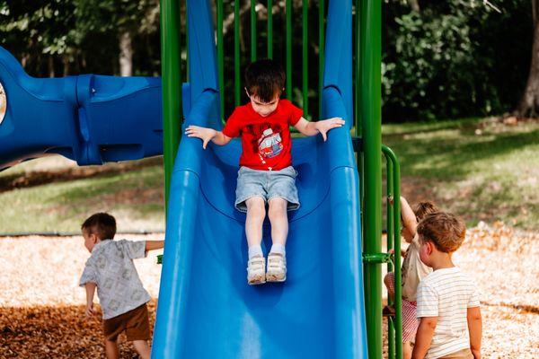 Child having fun on Foundations Preschool playground slide.