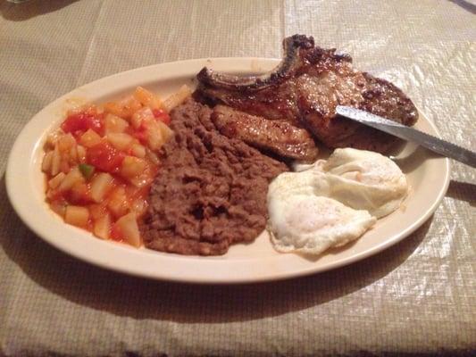 Pork Chop and eggs with a side of Papas a la Mexicana and Refried Beans.