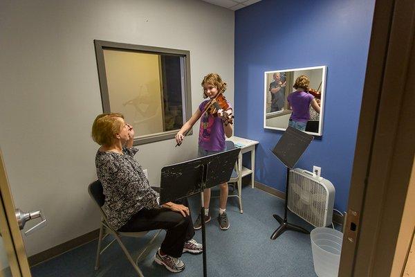 Instructor Carrie Grams looks on as Katie S plays her violin. Her bowhold is perfect, and Miss Carrie compliments her fingering.