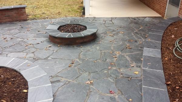 Slate stone patio with seat wall, raised planters, gas fire pit, and lighting.