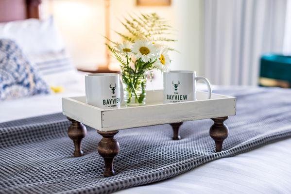 two Bayview Hotel brand mugs sit on either side of a small floral centerpiece on a wooden bed tray with four ornate legs