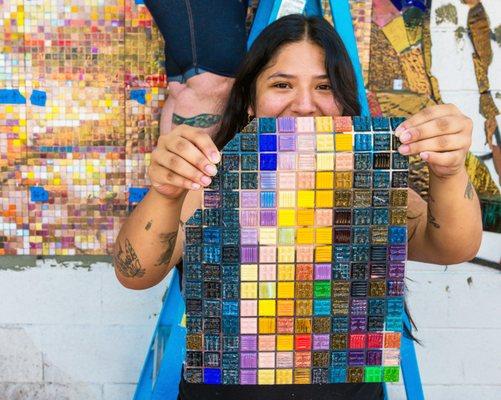 Co-founder Carmen Rangel holds up a colorful section of glass mosaic tiles on installation day.