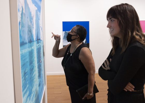 Two women looking closely at an artwork hanging on the wall.