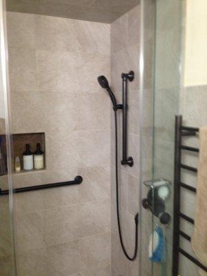 The finished steam room has grab support bars, an inset shampoo holder, glass to the ceiling