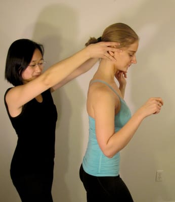 I help my student lengthen her whole body by subtly adjusting the relationship between her head and her spine.