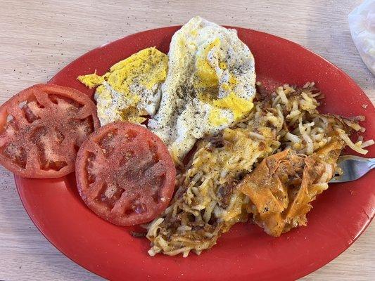 Fried eggs over hard with shredded hash browns with cheese and side tomatoes