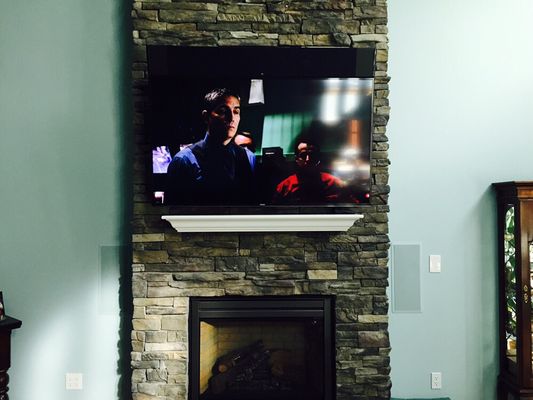 TV over stone fireplace with TV mounted center channel speaker & in-wall left & right channel speakers