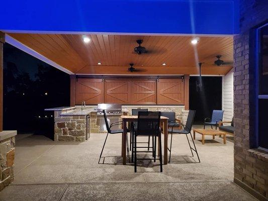 This patio cover features a tongue & groove ceiling, custom sliding barn doors, composite decking and an outdoor kitchen.