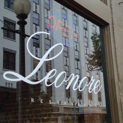 Close-up of the Leonore window sign with a reflection of the building across the street.