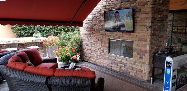 TV installed on stone above fireplace in patio area