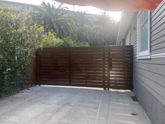 Wooden and iron automatic car gate with pedestrian side gate, stained in dark brown.