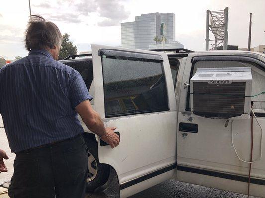 The dog  is kept inside of a suburban with a window unit.