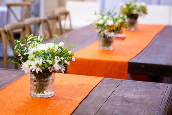 Several arrangements spread along orange runners on wooden tables. Looked very upscale but achieved with modest budget thanks to Monique!