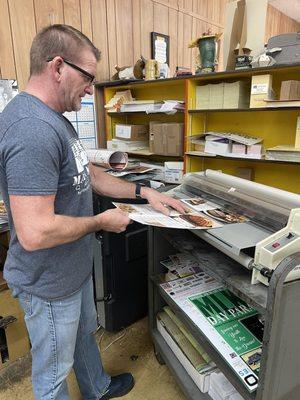 Pressman and co-owner Andy Mars laminating full color restaurant menus after printing them.