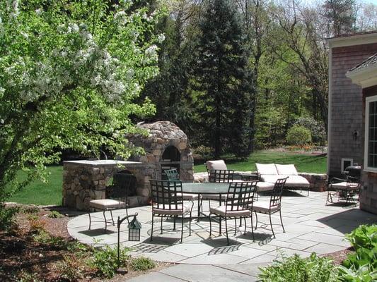 Backyard entertaining and dining area: feature custom fireplace, oven, fieldstone sitting walls, bluestone patio, lighting, and more.