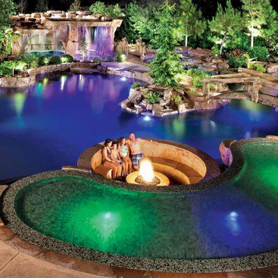 Lagoon-style concrete pool with integrated landscape pockets, sunken conversation area with fire pit, and multicolor LED lighting