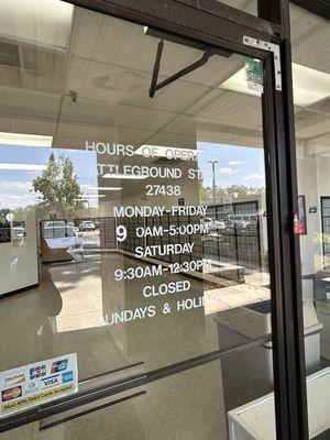 The front door with hours of operation of the USPS - Battleground Office in Greensboro, NC.