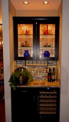 Bar with custom cabinets, lighting, and wine fridge.