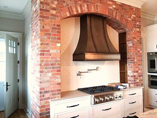 thin brick arch surround around the cooktop with a tile backsplash and copper vent