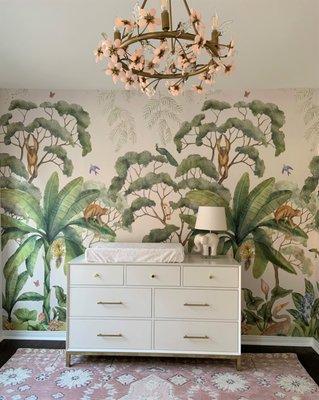 This beautiful nursery boasts a gorgeous jungle mural, a quartz flower chandelier, and modern furniture.