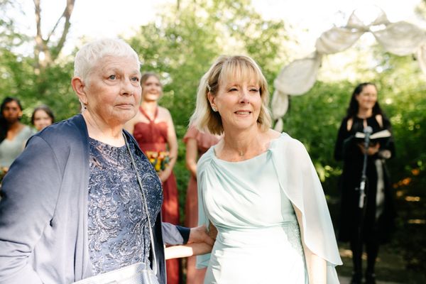 mom and grandma watch a bride walk down the aisle, with bridesmaids and officiant in the background all doing the same