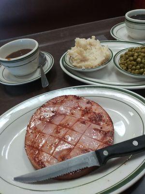 Virginia ham steak with gravy in separate cup. Mashed potatoes and peas.